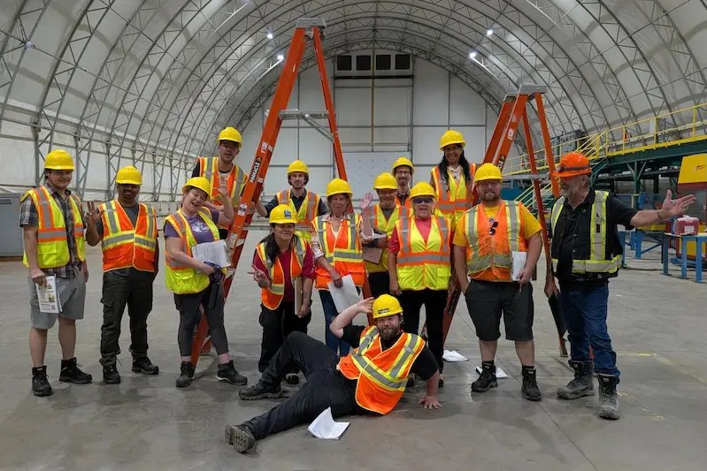 A group of IGV Housing workers in hard hats and safety vests posing inside the manufacturing facility