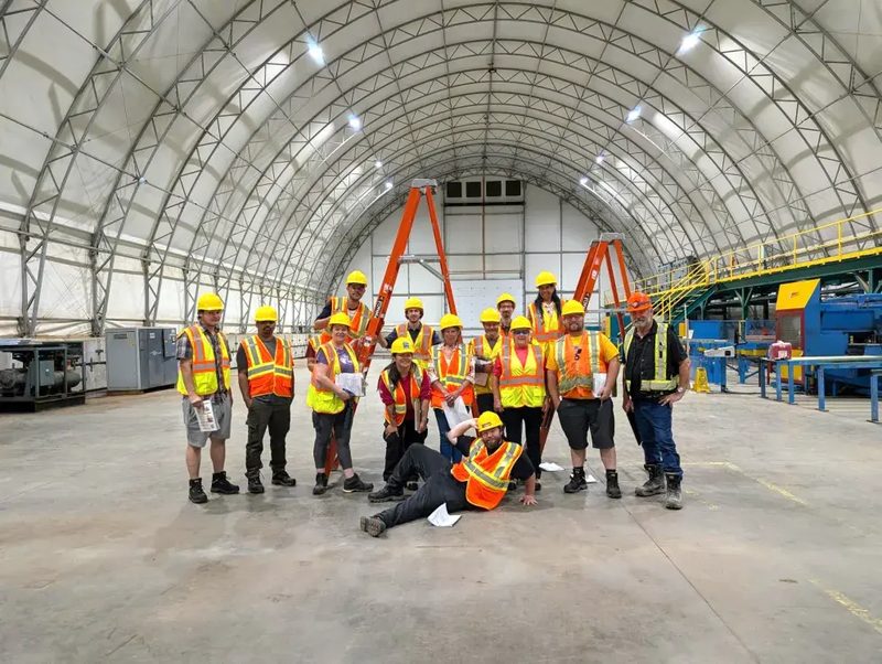 A group of IGV Housing workers in hard hats and safety vests posing inside the manufacturing facility
